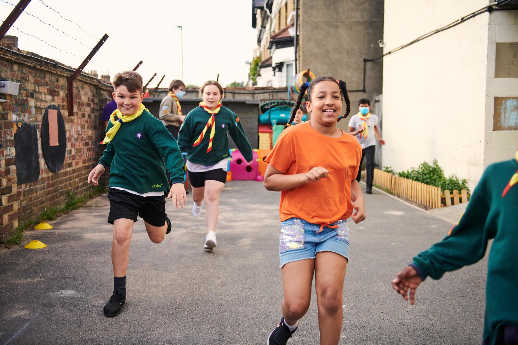 Children dressed in cubs uniforms running down an alleyway